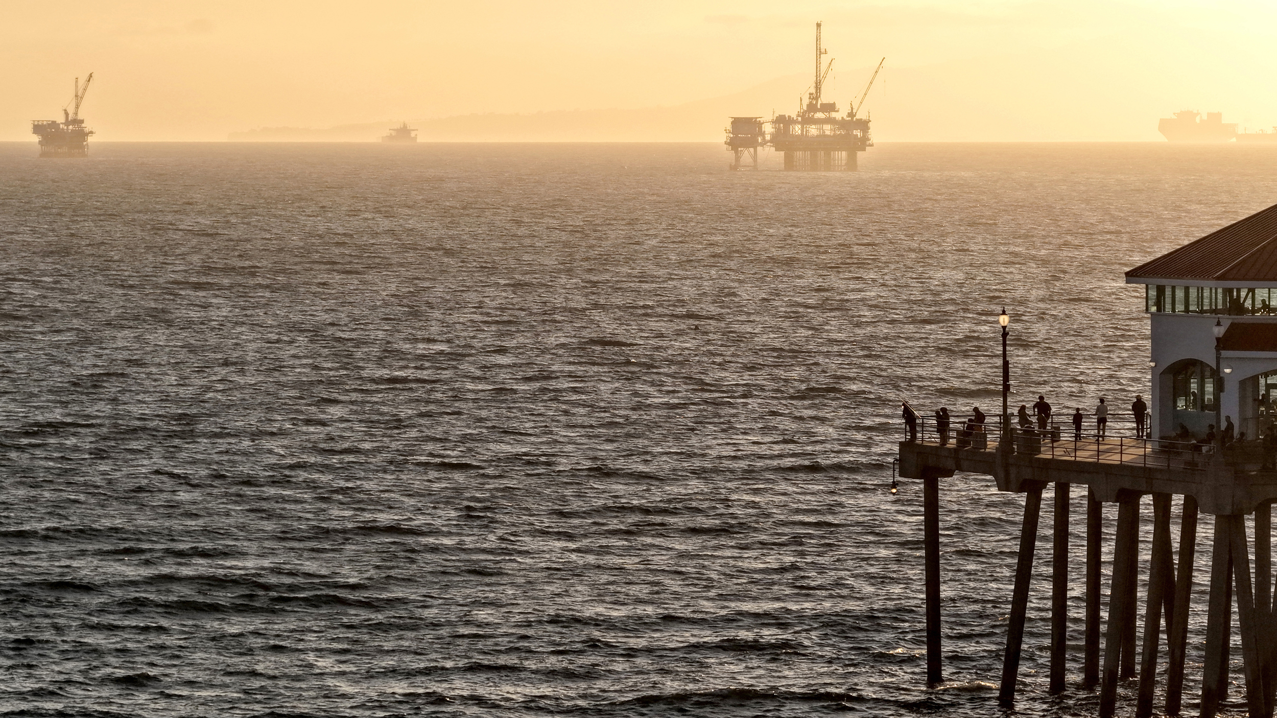 People stand on a pier with an offshore oil platform in the distance on July 1 in Huntington Beach, Calif. Credit: Mario Tama/Getty Images